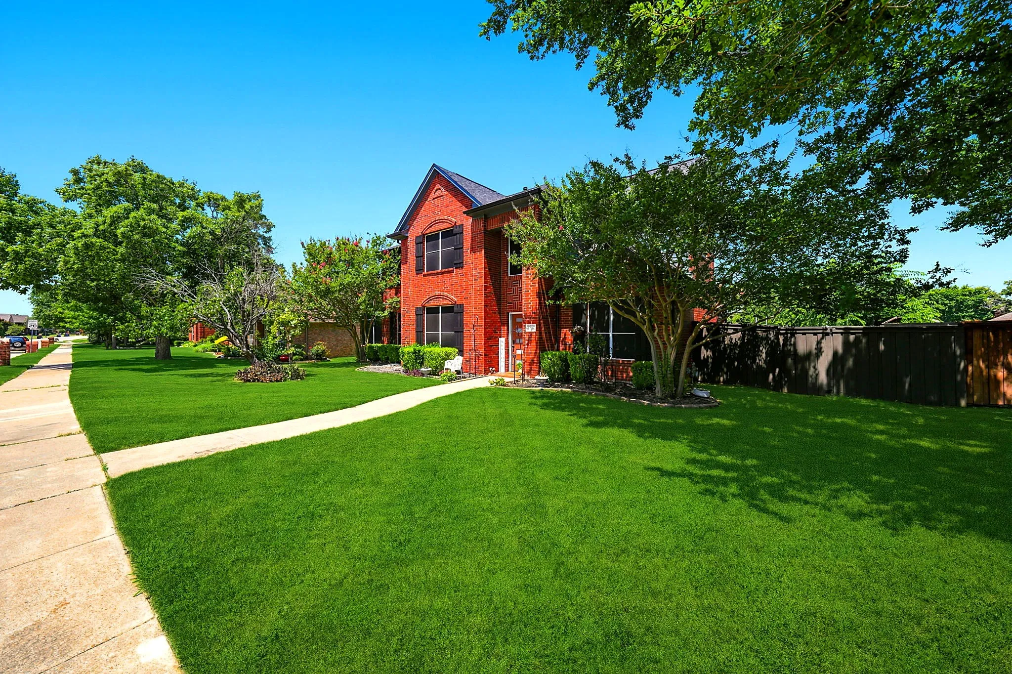 Brick exterior, two-story structure, dark roof, front yard with mature trees, established landscaping