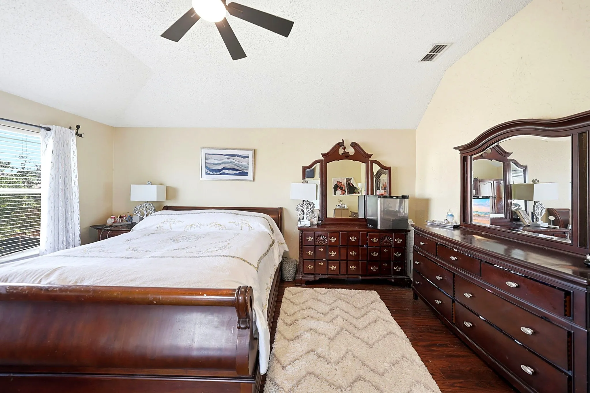 Vaulted ceiling, ceiling fan, wood-finish flooring, and window with blinds