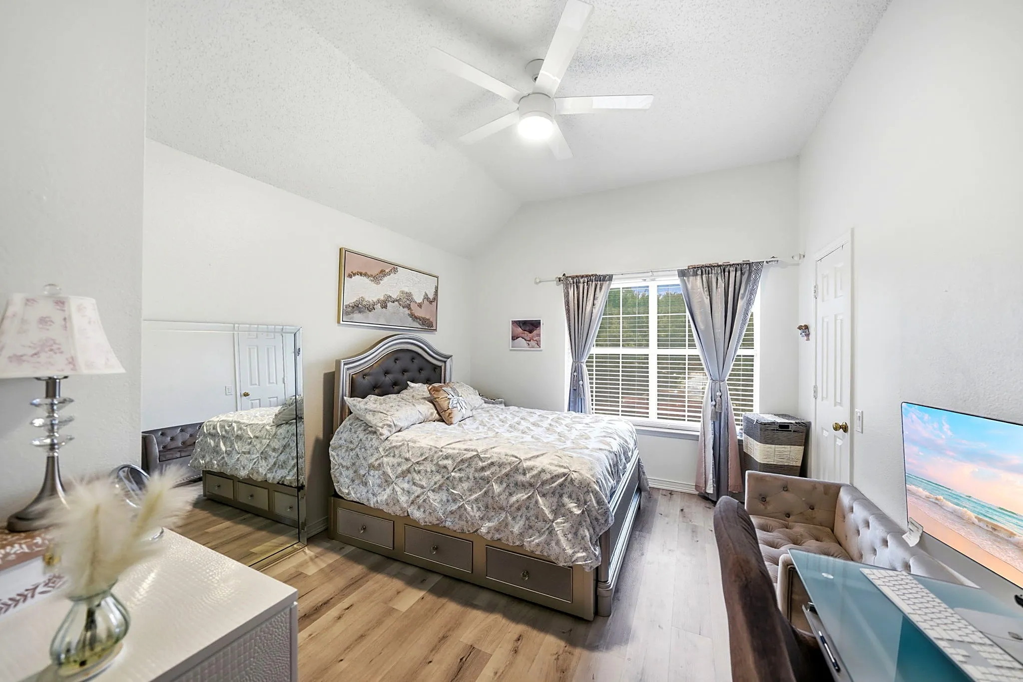 Vaulted ceiling, ceiling fan, wood-finish flooring, window with blinds, white paneled door