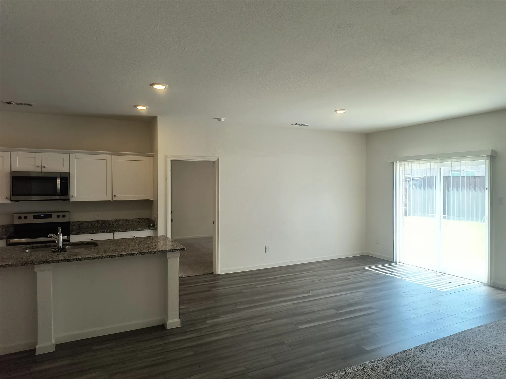 Open-concept layout with wood-finish flooring, white cabinetry, granite countertops, and stainless steel appliances