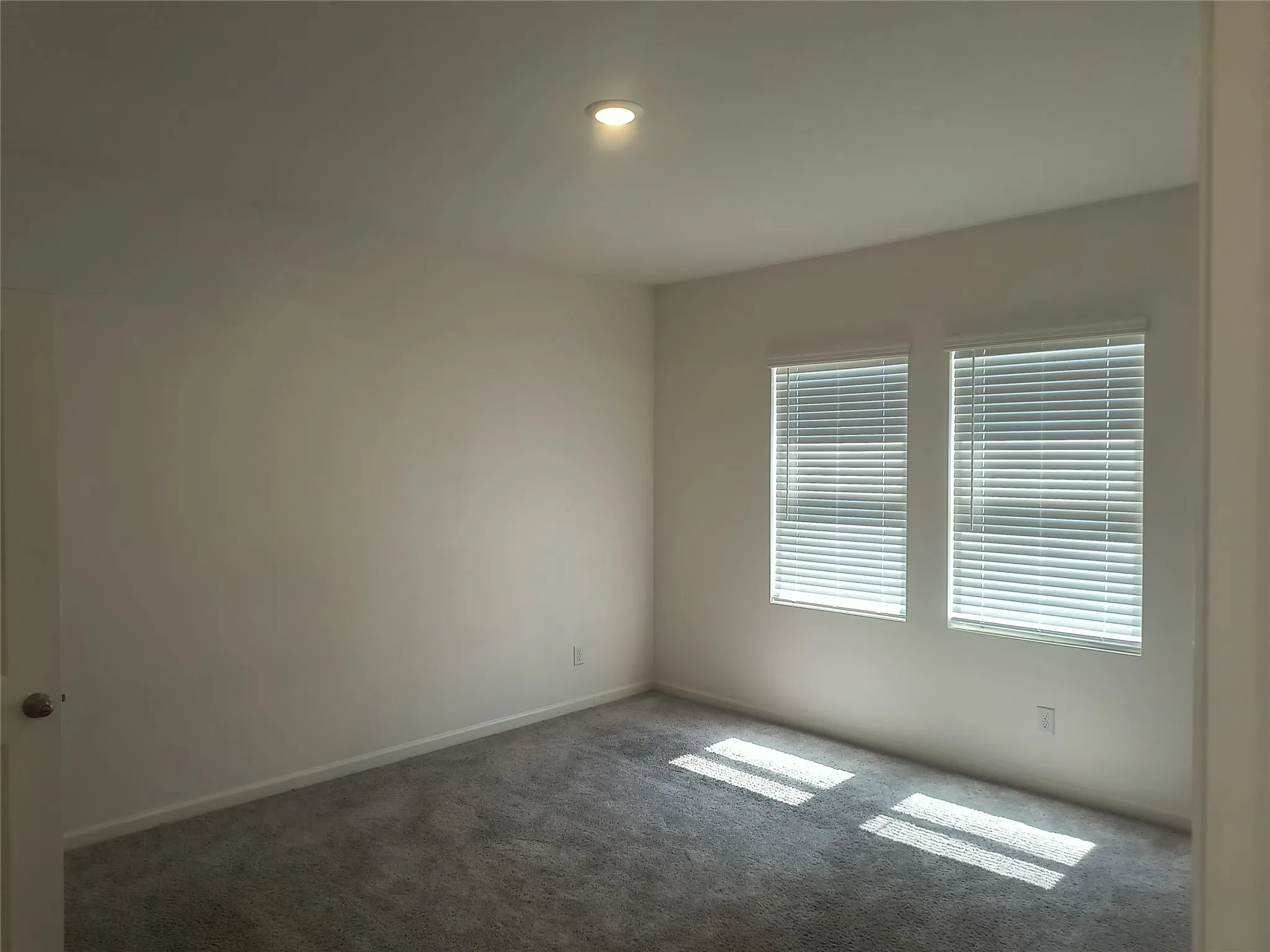 Recessed ceiling lighting, gray carpeting, two windows with blinds