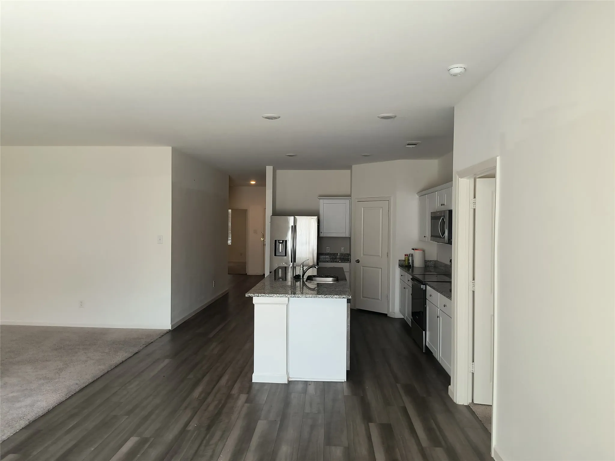 Open-concept kitchen with a central island, stainless steel refrigerator, white cabinetry, and a built-in microwave