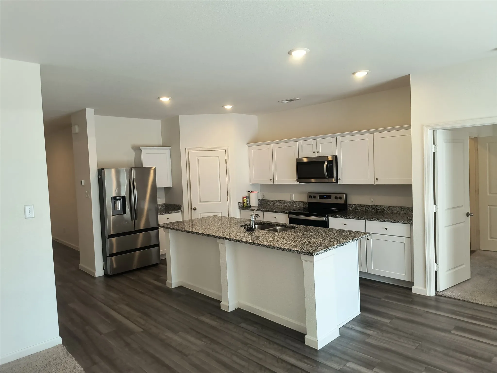 Kitchen with granite countertops, stainless steel appliances, white cabinetry, a center island with sink, and recessed lighting