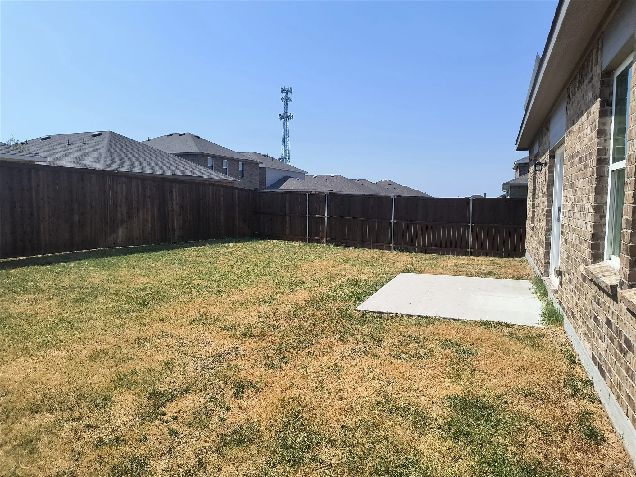 Backyard featuring a privacy fence, concrete patio, and brick exterior