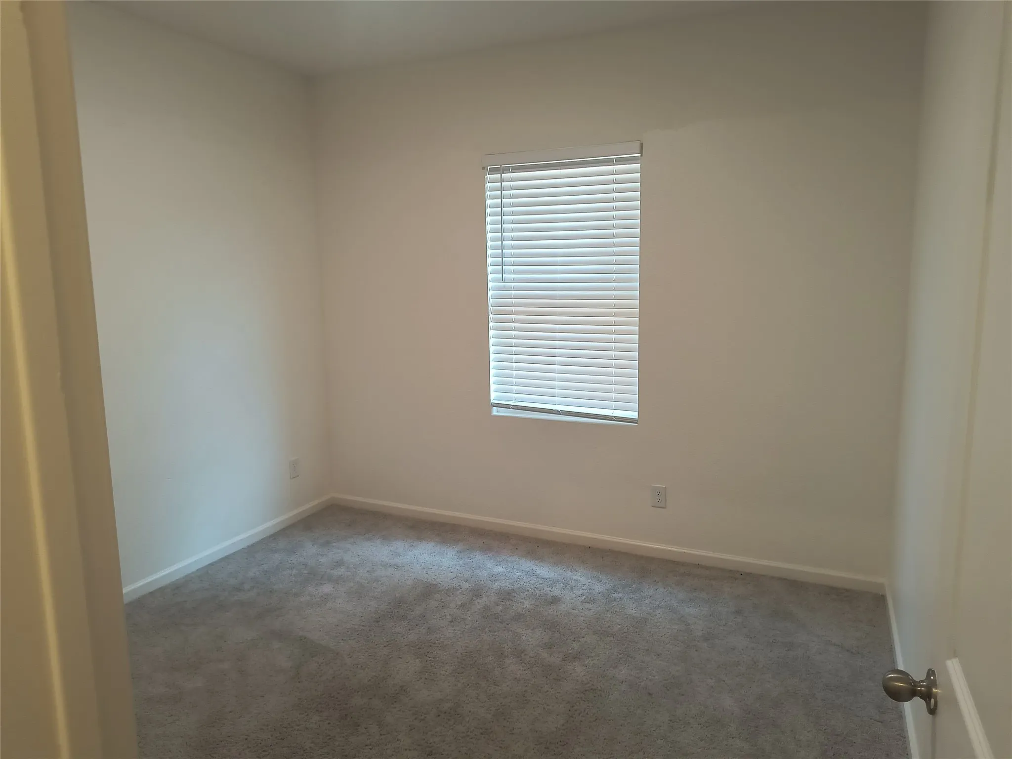 Room featuring neutral-toned walls, carpeted flooring, and a window with horizontal blinds