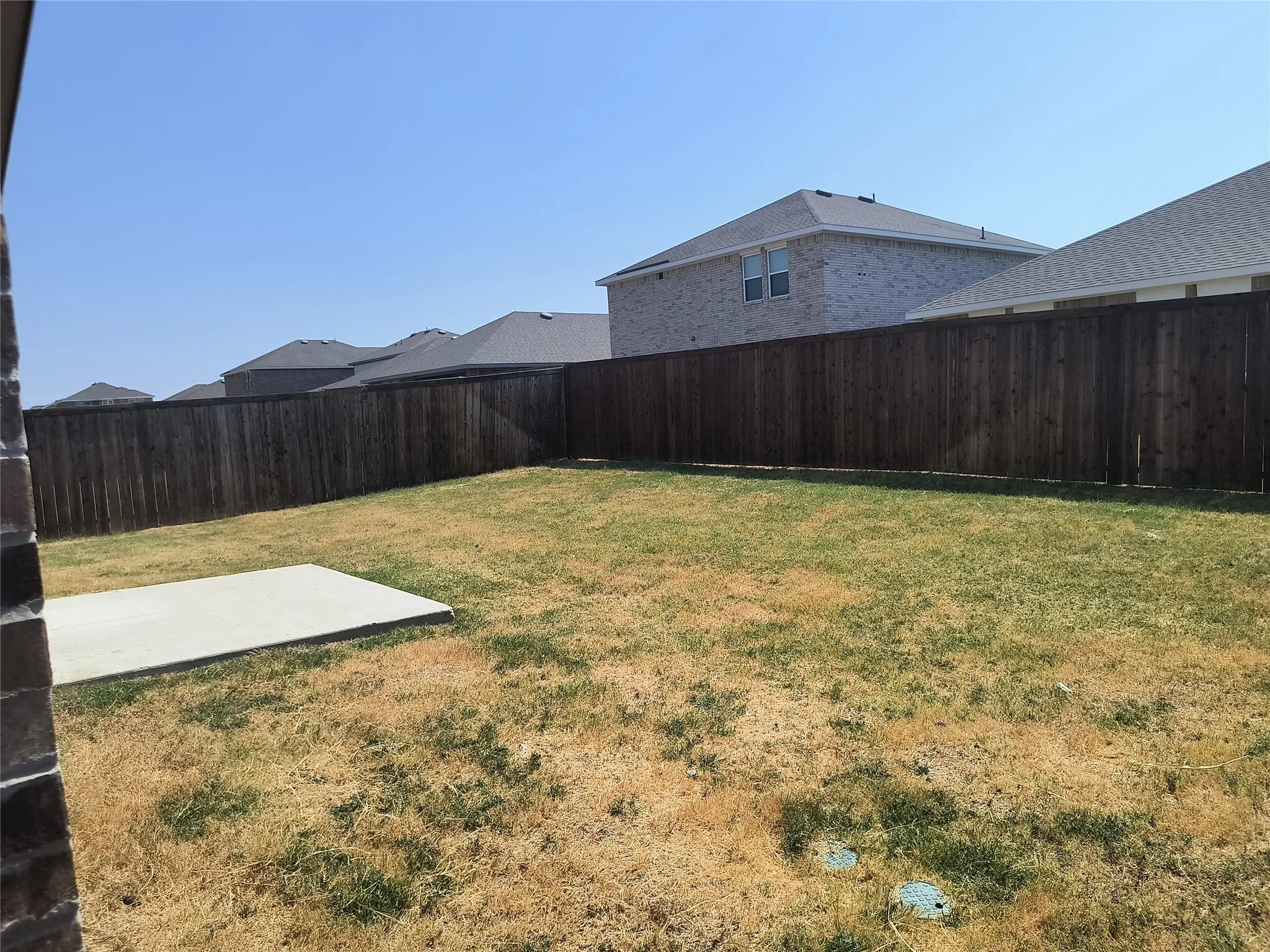 Expansive backyard featuring a privacy fence, concrete patio, and a grass lawn