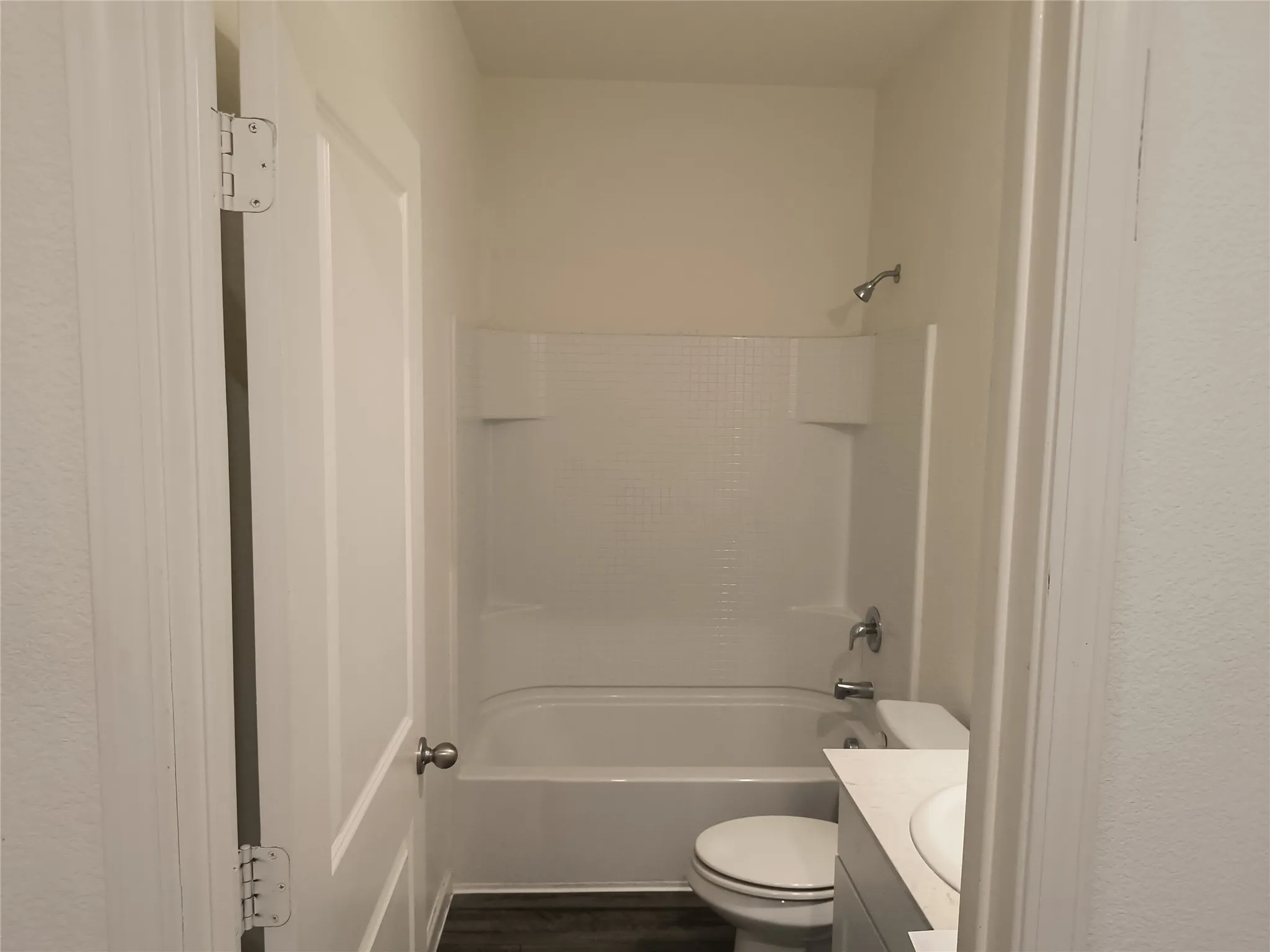 White tub and shower combination with shower head, toilet, vanity with integrated sink, and wood-finish flooring