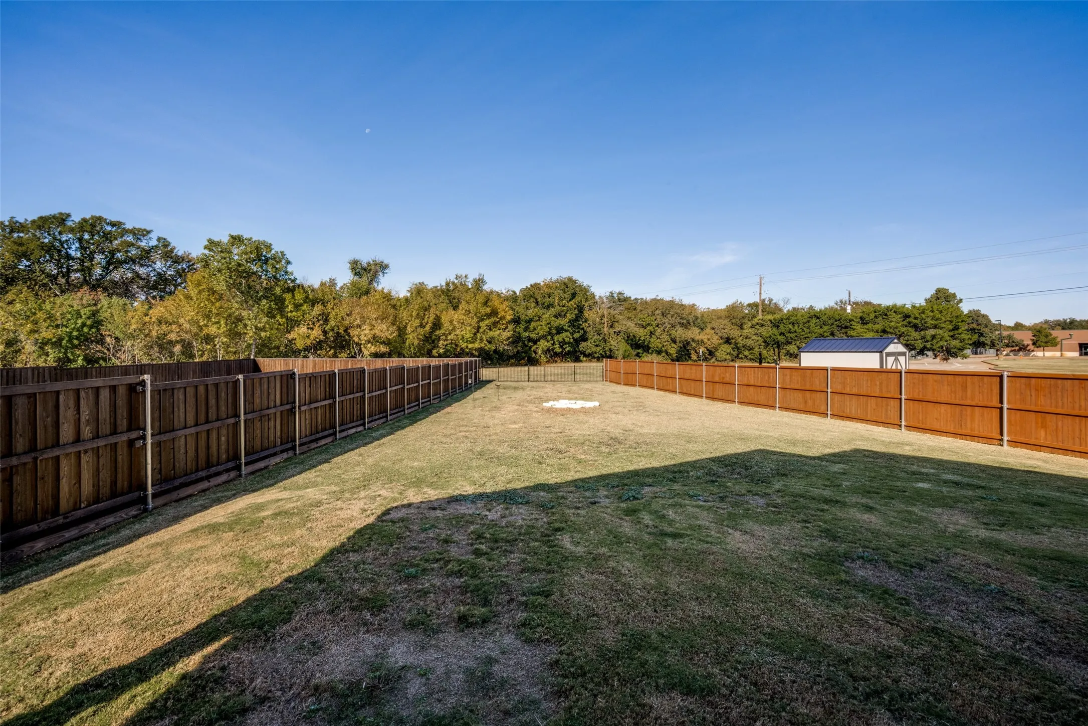 Expansive backyard featuring a manicured lawn, wood-paneled perimeter fencing, and a detached storage shed