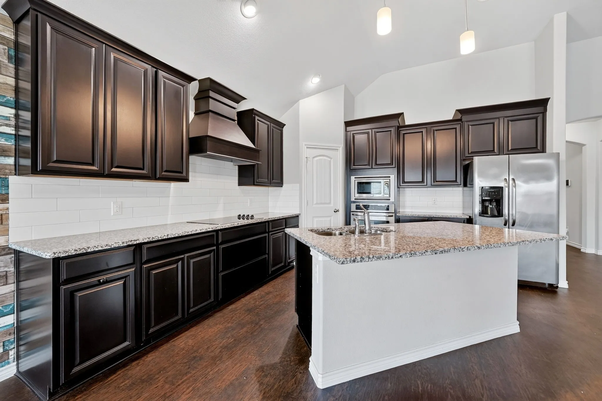 Kitchen featuring dark wood-finish cabinetry, granite countertops, stainless steel appliances, and a central island with an undermount sink