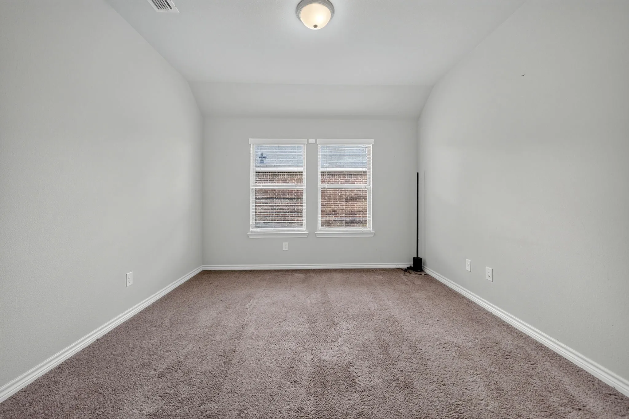 Neutral-toned walls, plush carpeting, double windows, and a ceiling-mounted light fixture