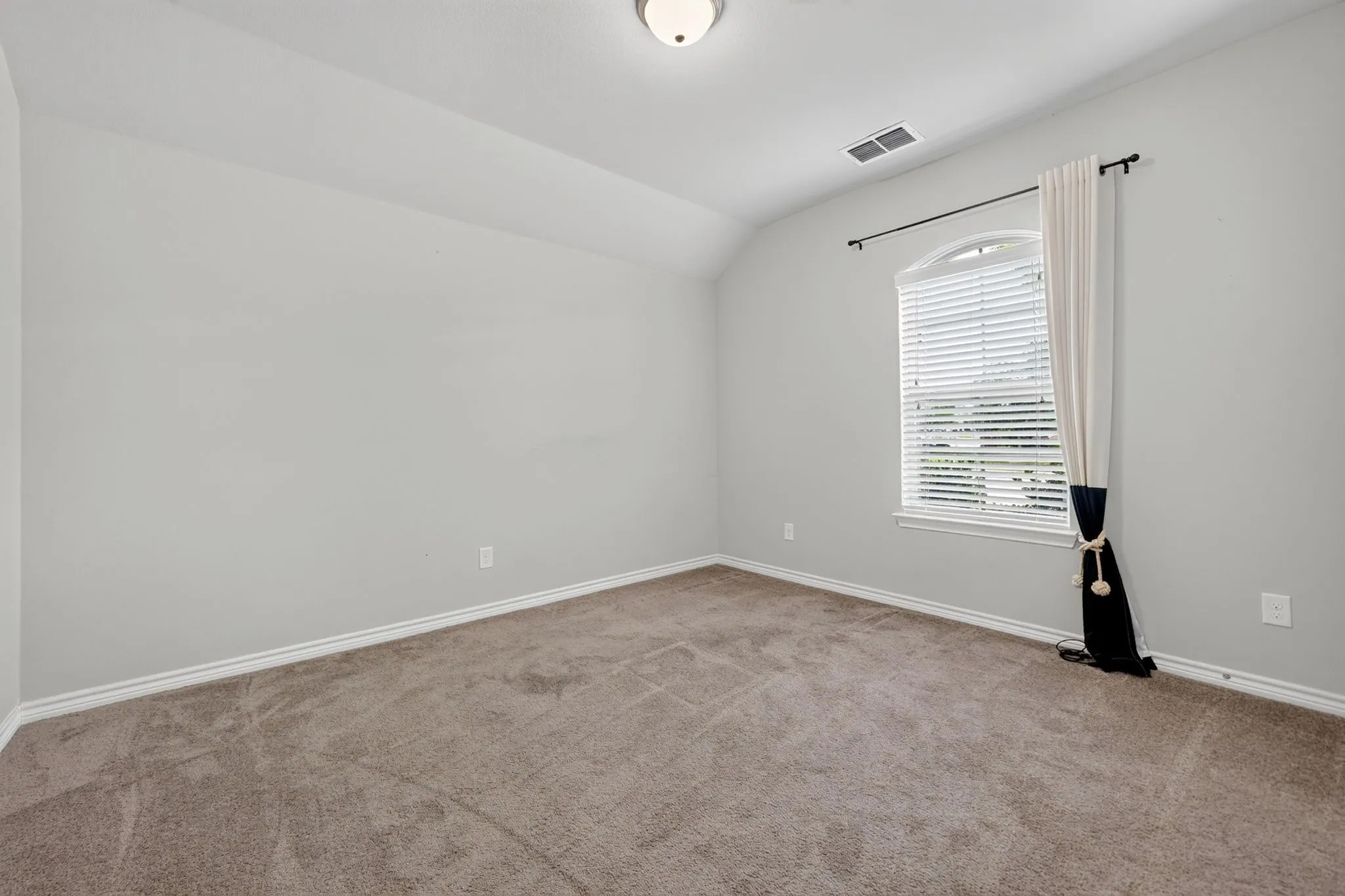 Carpeted room with a vaulted ceiling, an arched window, and a flush mount ceiling light fixture