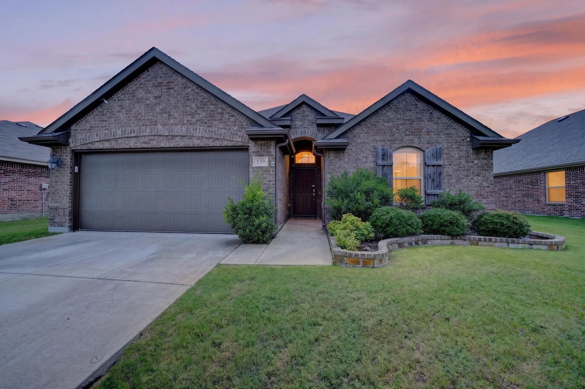 Brick exterior with a gabled roofline, concrete driveway, stone-edged landscaping, and a covered entryway