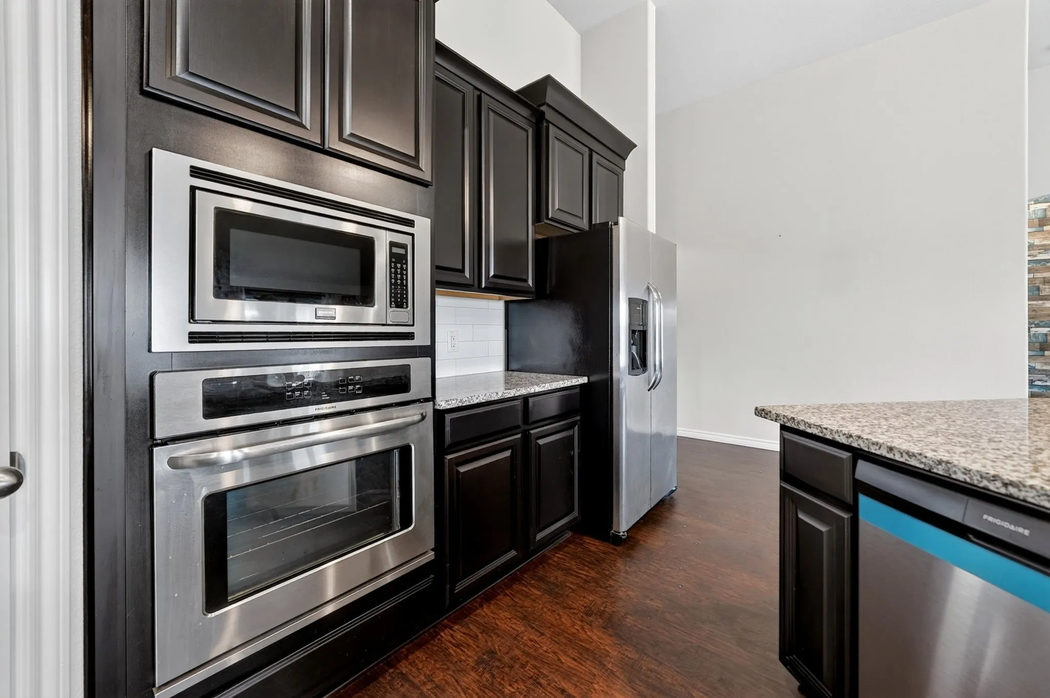 Stainless steel appliances, built-in microwave, dark wood-finish cabinetry, granite countertops, and wood-finish flooring