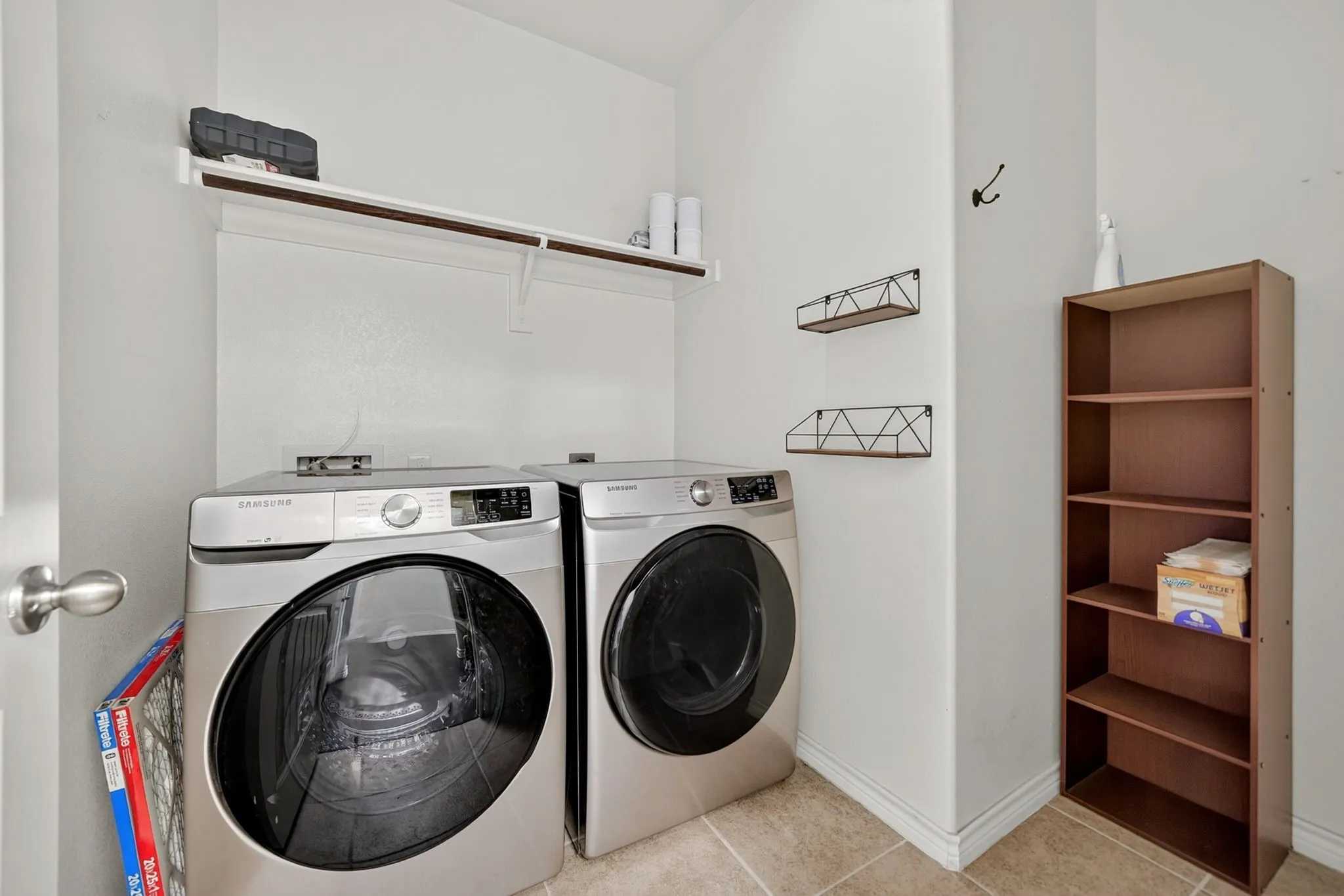 Laundry area with tiled flooring, an upper shelf, and an additional storage unit
