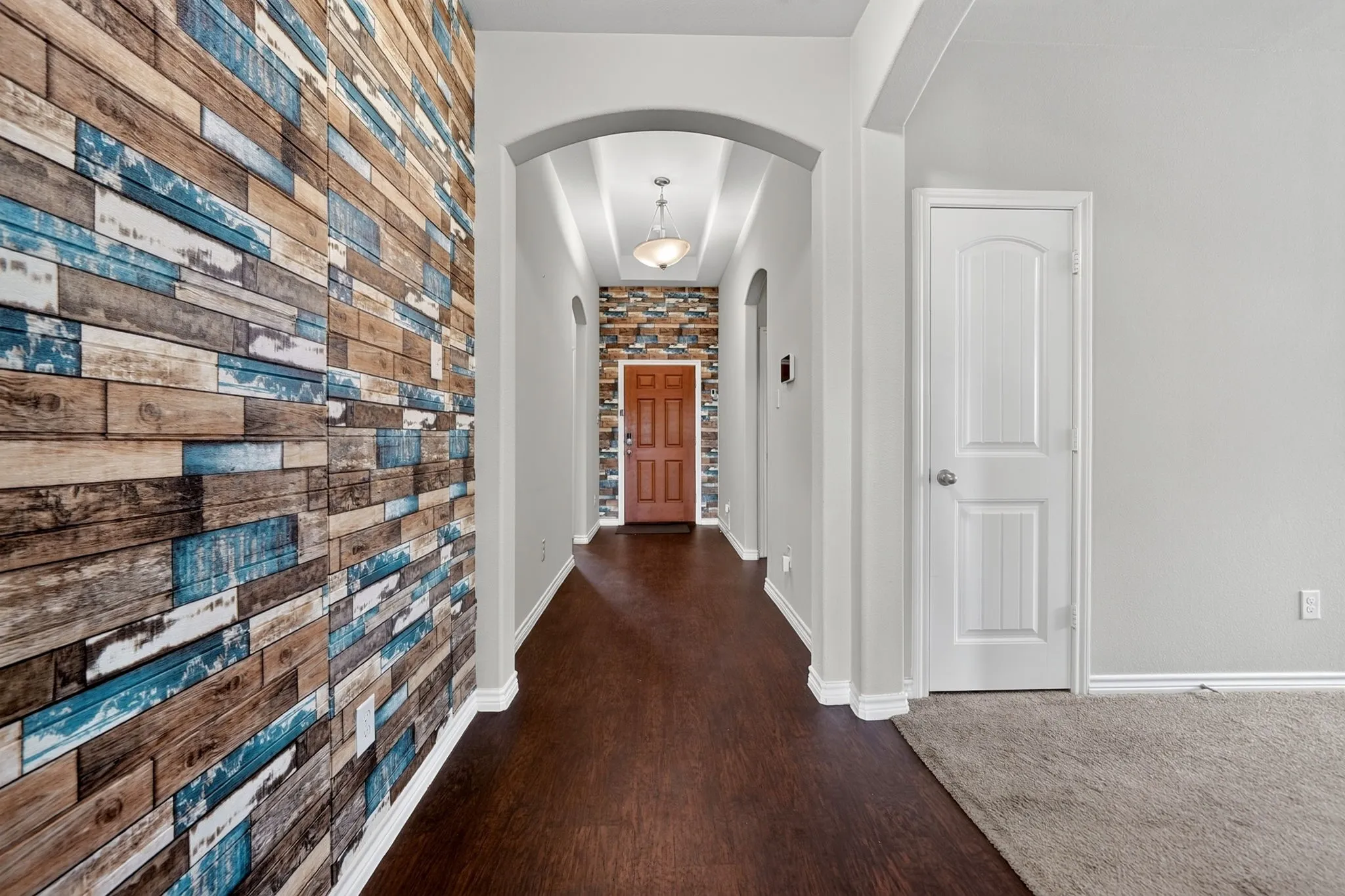 Entryway featuring wood-finish flooring, an arched doorway, and a decorative accent wall