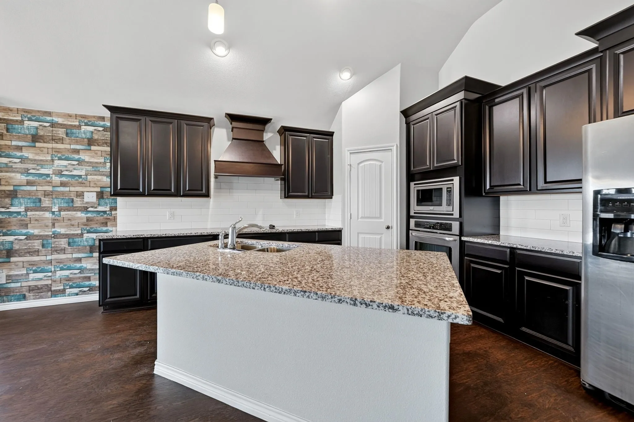 Kitchen featuring dark wood-finish cabinetry, granite countertops, stainless steel appliances, and a central island with an undermount sink