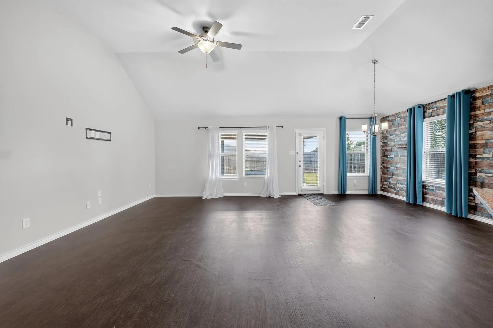 Vaulted ceiling, wood-finish flooring, ceiling fan, accent wall with stacked stone, and multiple windows