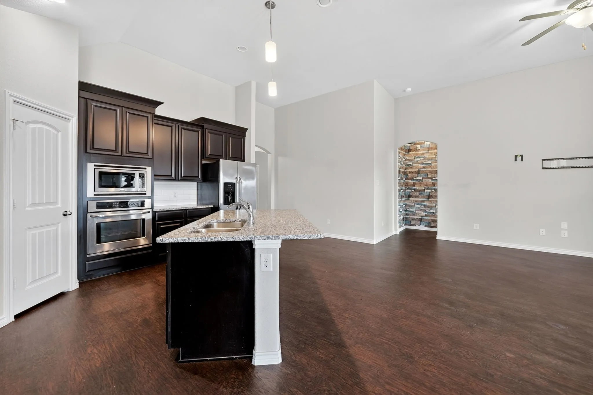 Open-concept living area with wood-finish flooring, vaulted ceilings, and a stone-clad arched entryway