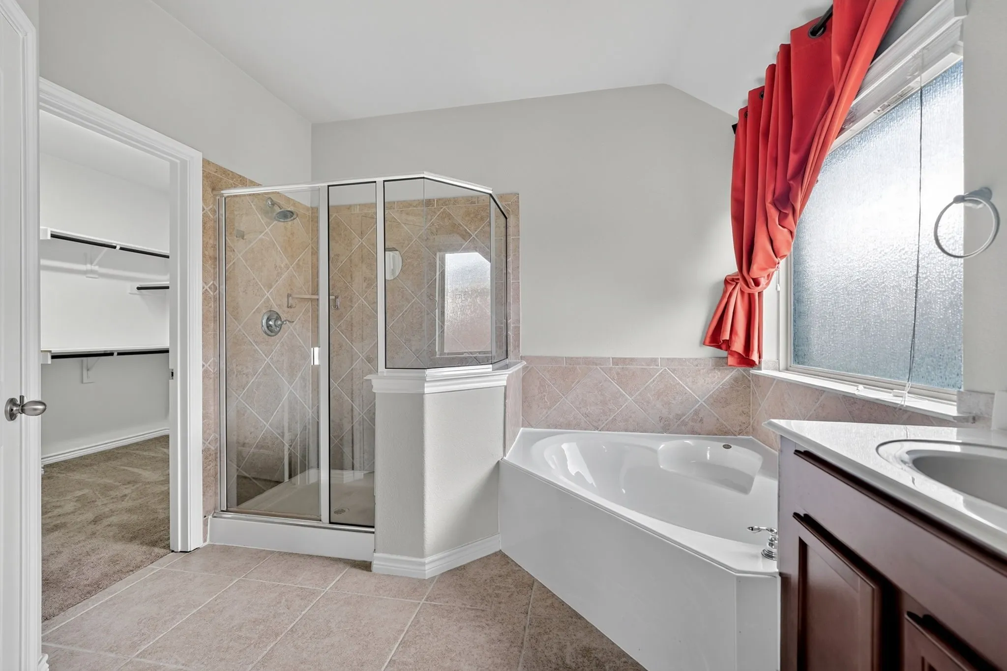 Corner soaking tub with tile surround, glass-enclosed shower with tile, double vanity with integrated sinks, and built-in closet shelving
