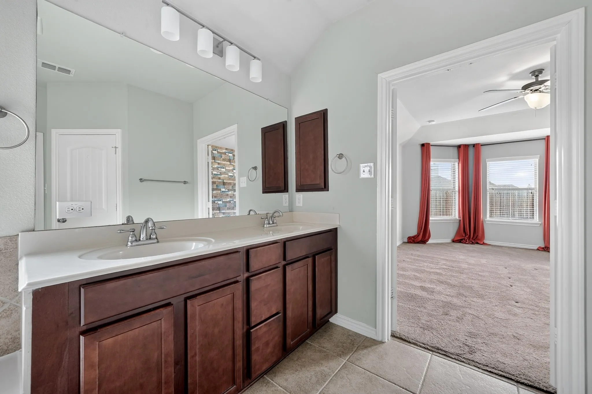 Dual vanity with undermount sinks and chrome fixtures, extensive wall mirror, track lighting, and tiled flooring