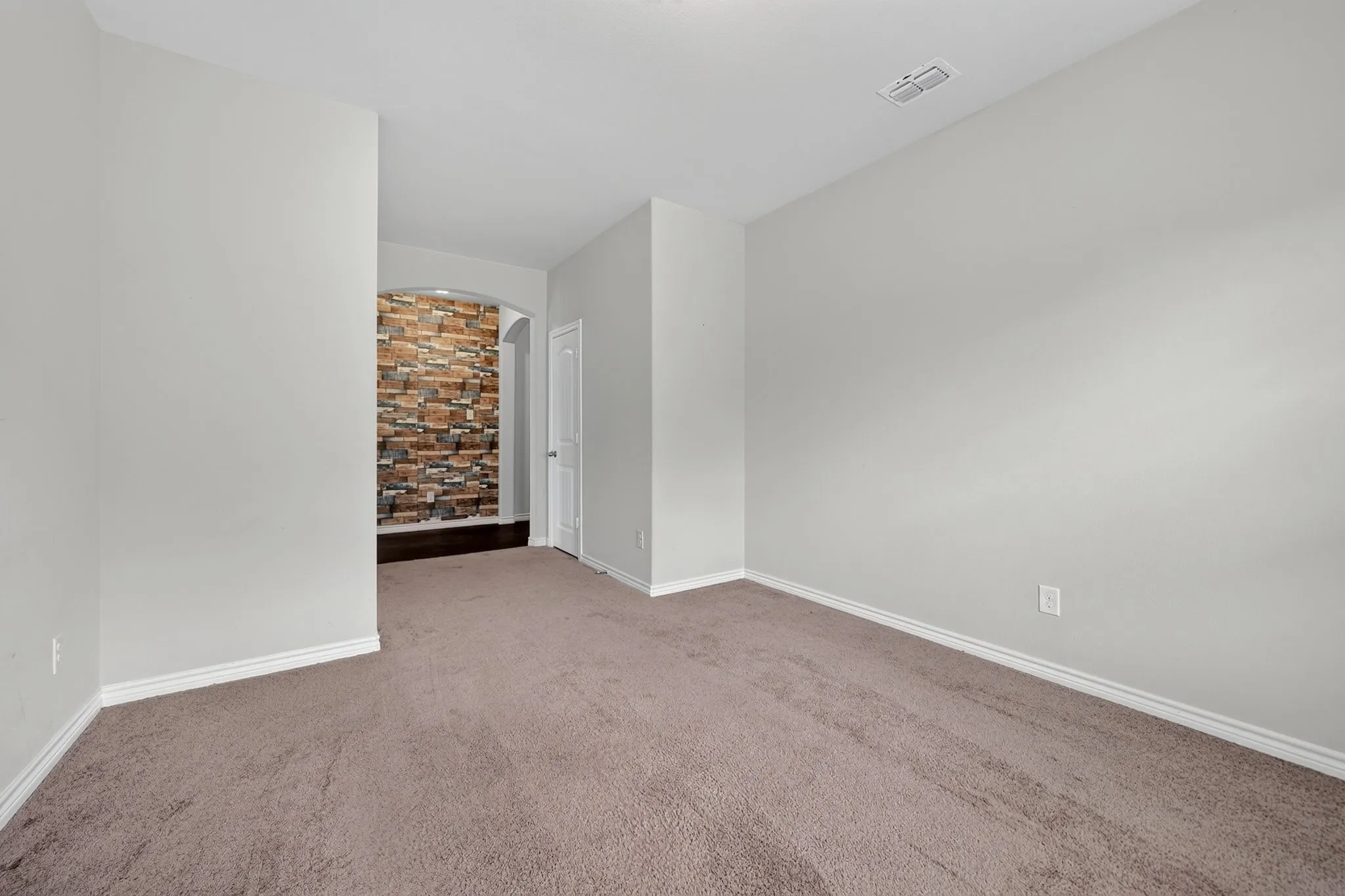 Spacious room with plush carpeting, neutral wall finishes, and an arched doorway leading to a decorative stone accent wall