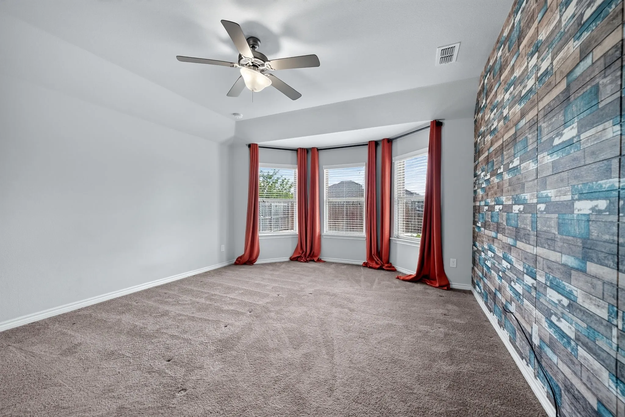 Tray ceiling with a ceiling fan, bay window with blinds, and textured accent wall