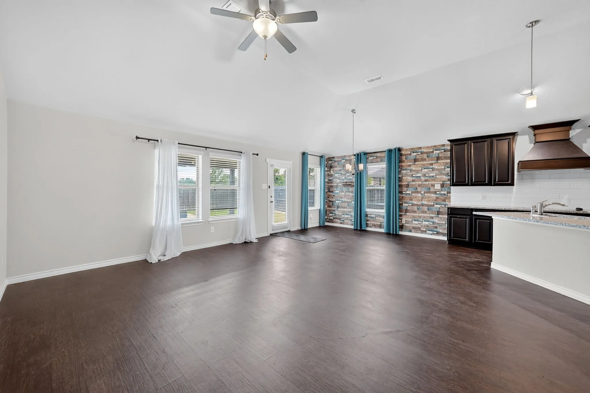 Vaulted ceiling with a ceiling fan, dark wood-finish flooring, kitchen with dark wood cabinetry, white subway tile backsplash, and a built-in range hood