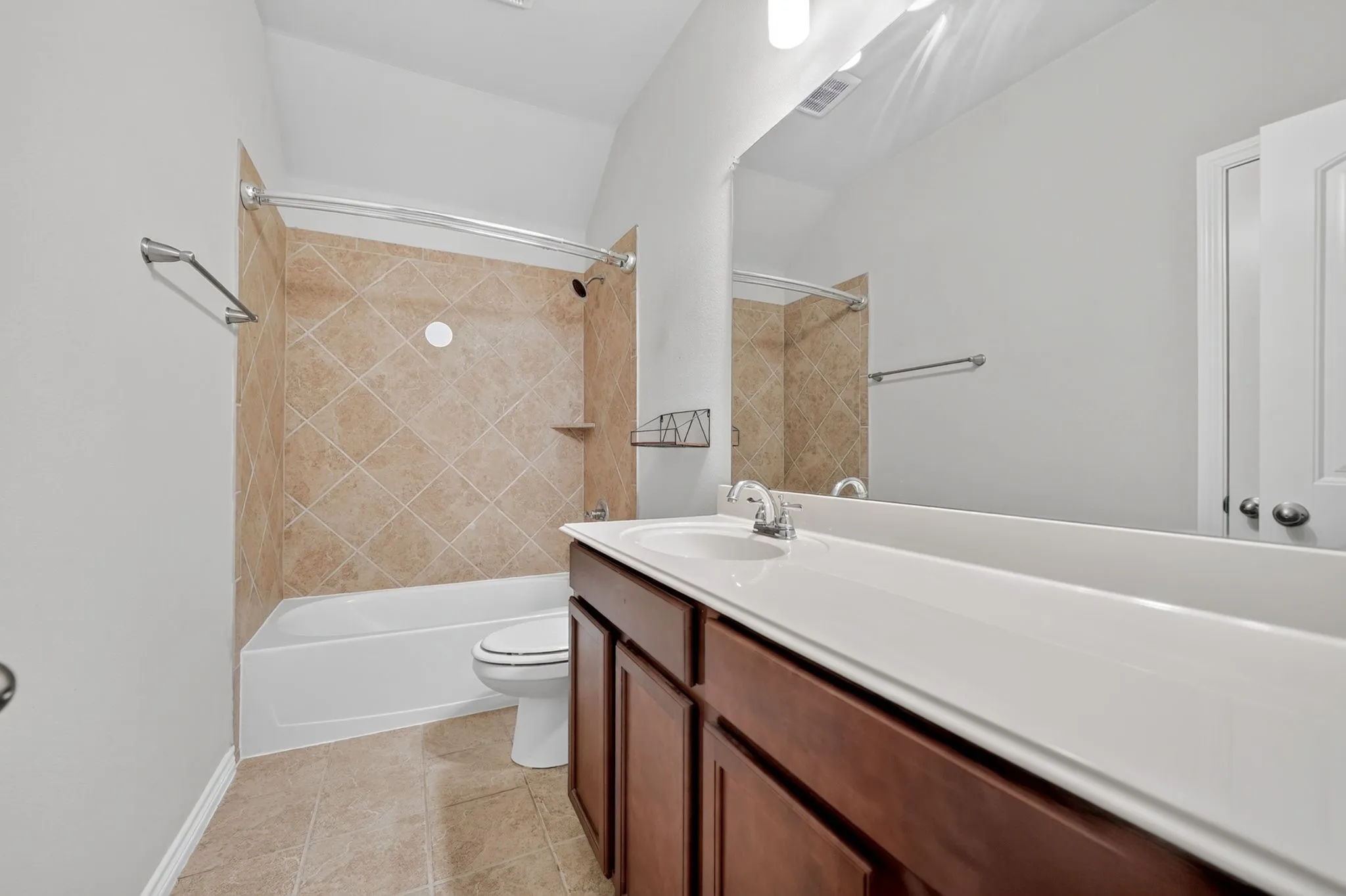 Integrated bathtub with tile surround, vanity with wood-finish cabinetry, single basin sink, and an expansive wall-mounted mirror