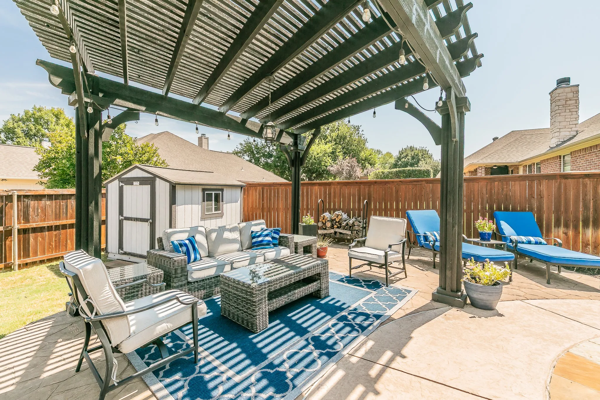 Concrete patio featuring a dark wood pergola with string lighting