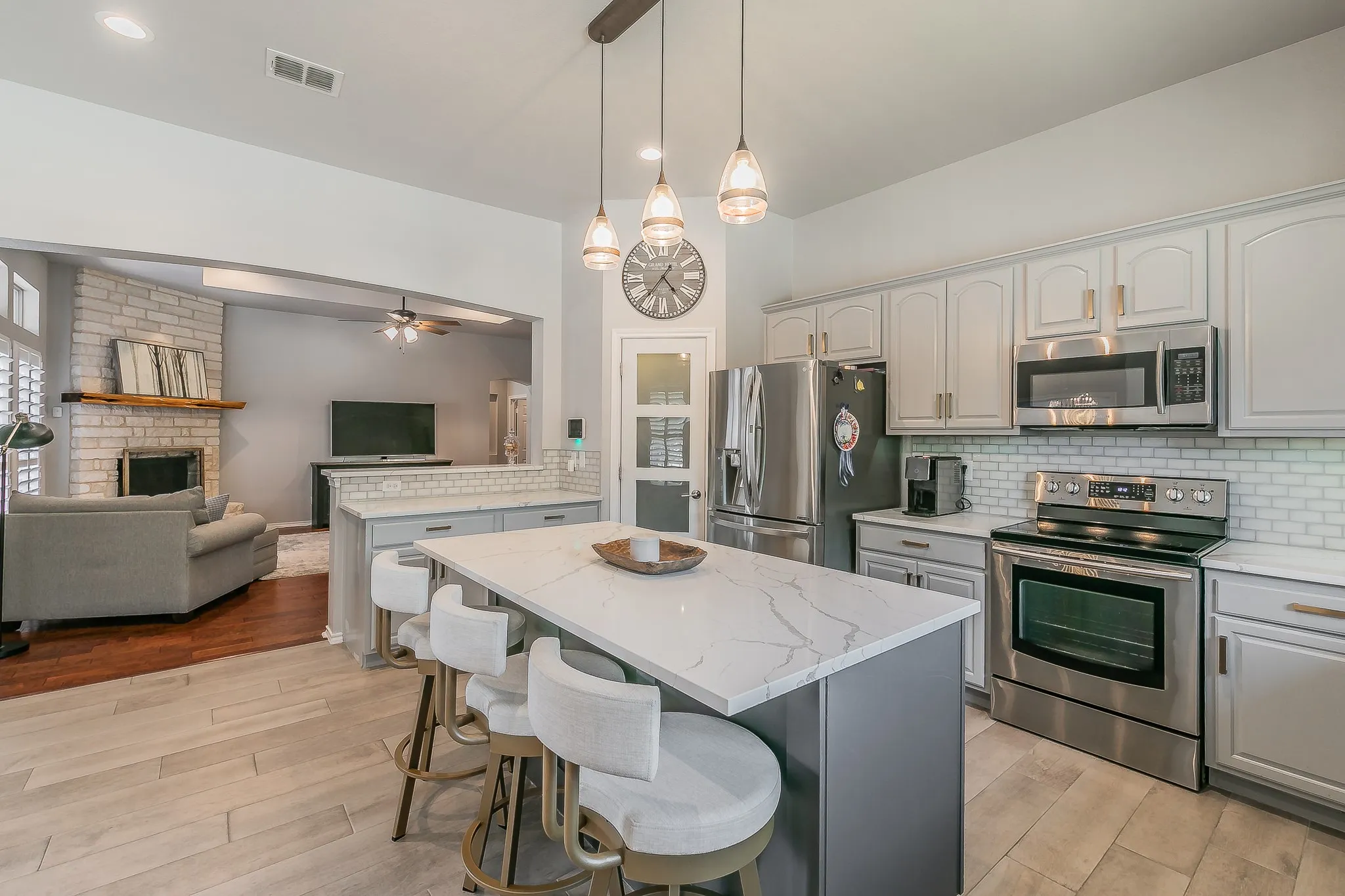 Kitchen with an expansive island featuring a quartz countertop, stainless steel appliances, light gray cabinetry, and subway tile backsplash