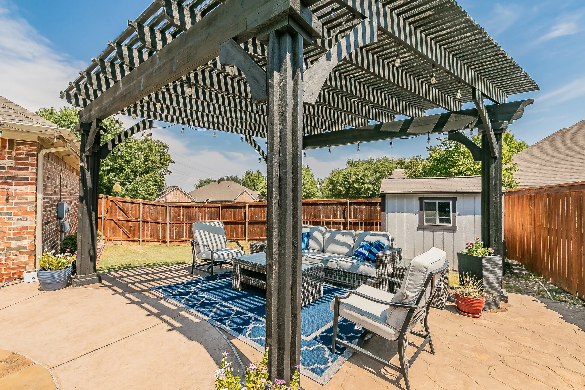 Stamped concrete patio featuring a dark wood pergola with string lights, enclosed by a wood privacy fence