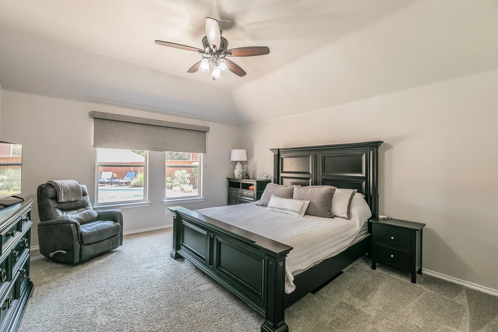 Vaulted ceiling, ceiling fan with light fixture, carpeted flooring, two windows, and roller shades
