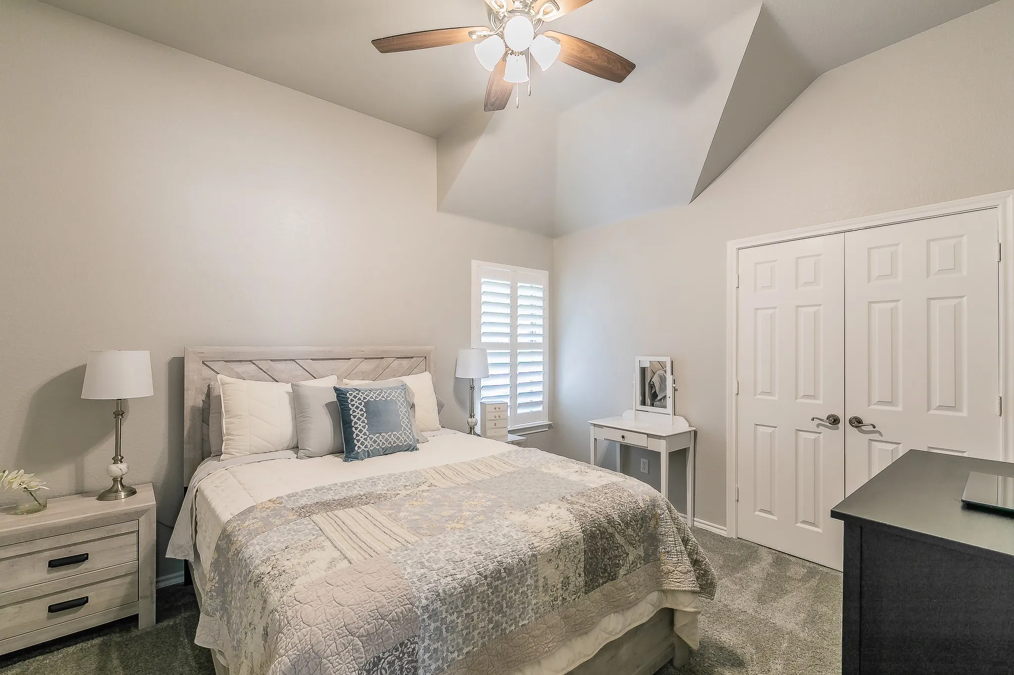 Vaulted ceiling with a ceiling fan, window with white plantation shutters, double-door closet, and carpeted flooring