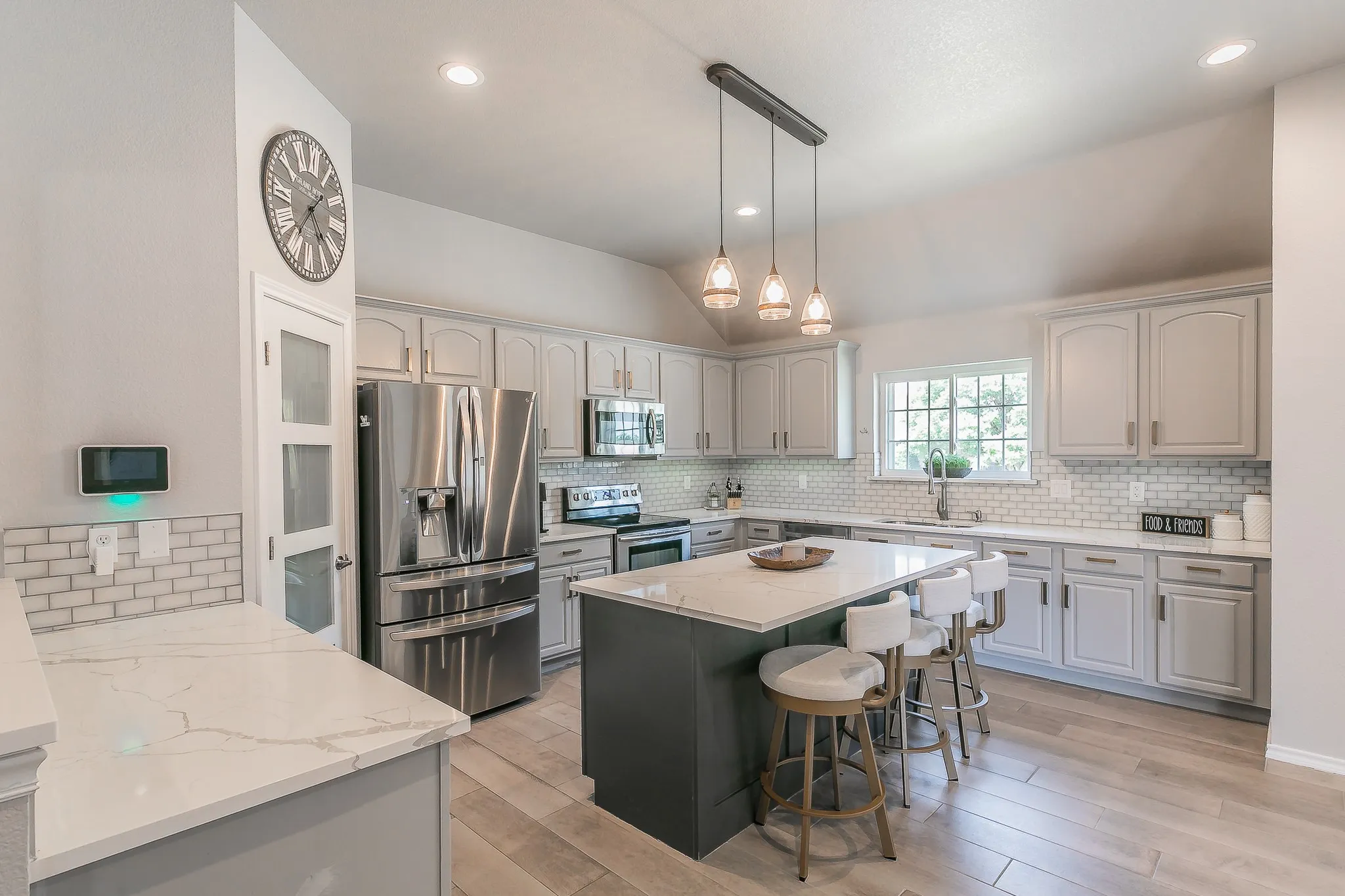 Kitchen featuring light-toned cabinetry, stainless steel appliances, a center island with a stone countertop, an undermount sink, and wood-finish flooring