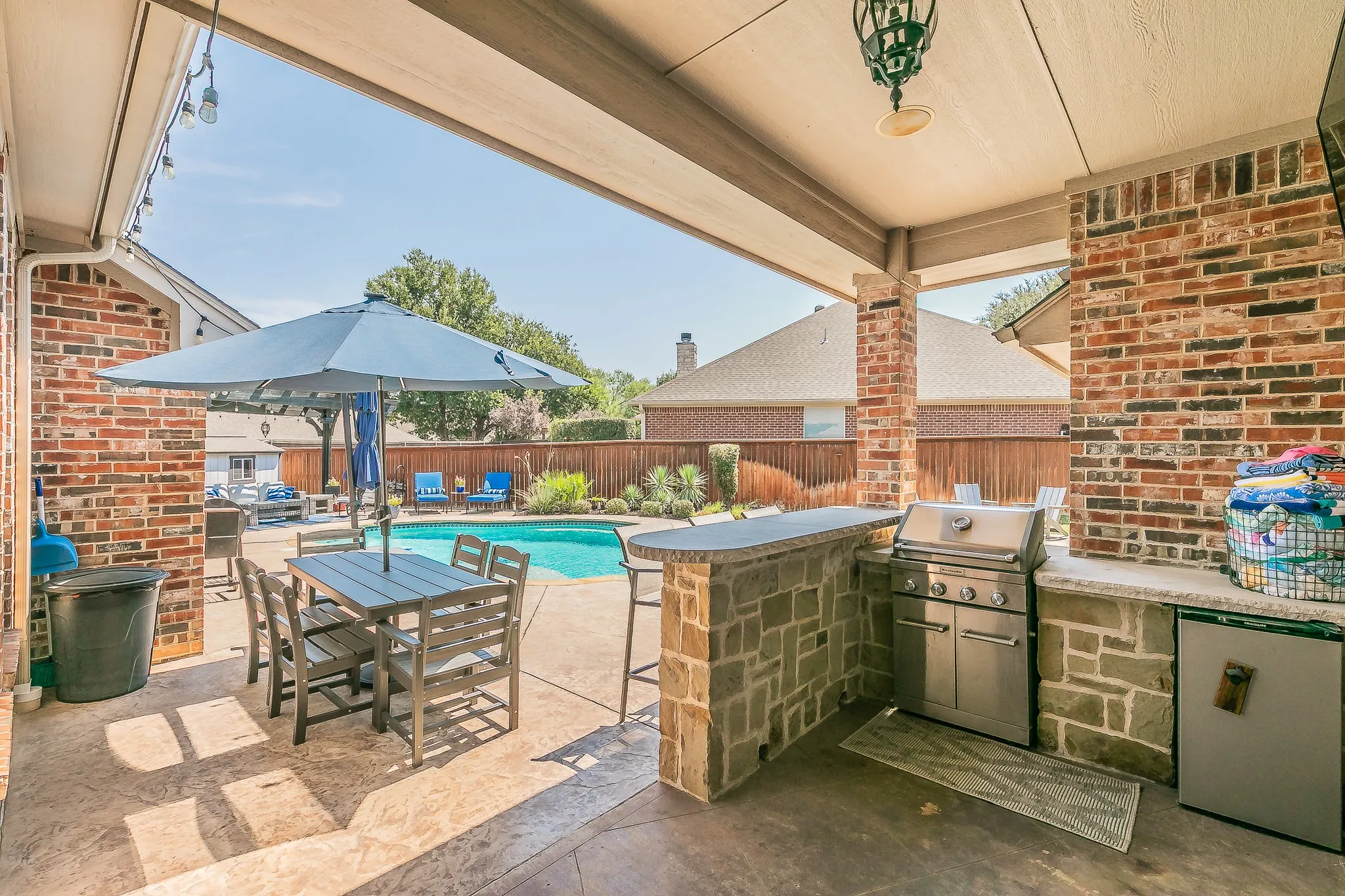 Covered patio with a built-in outdoor kitchen, stainless steel grill, beverage refrigerator, and stone-finish bar