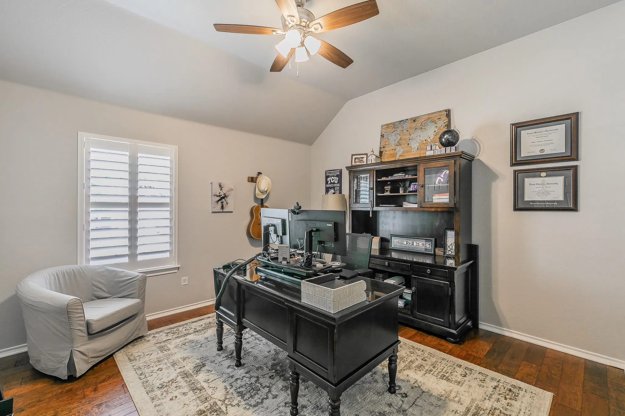 Vaulted ceiling with a ceiling fan, hardwood flooring, window with white plantation shutters, and light gray wall paint