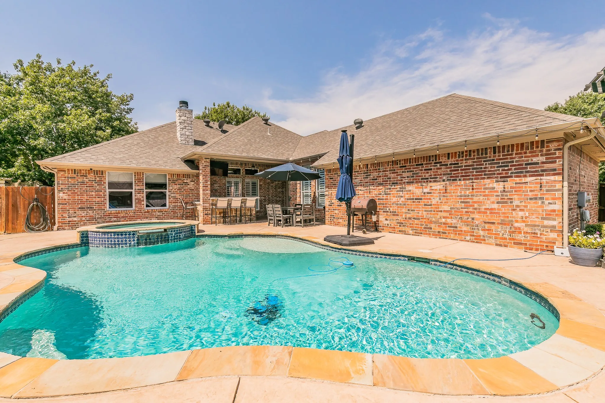 Brick exterior with a gabled roofline, featuring an integrated swimming pool, a tiled spa, and an outdoor patio bar with built-in seating