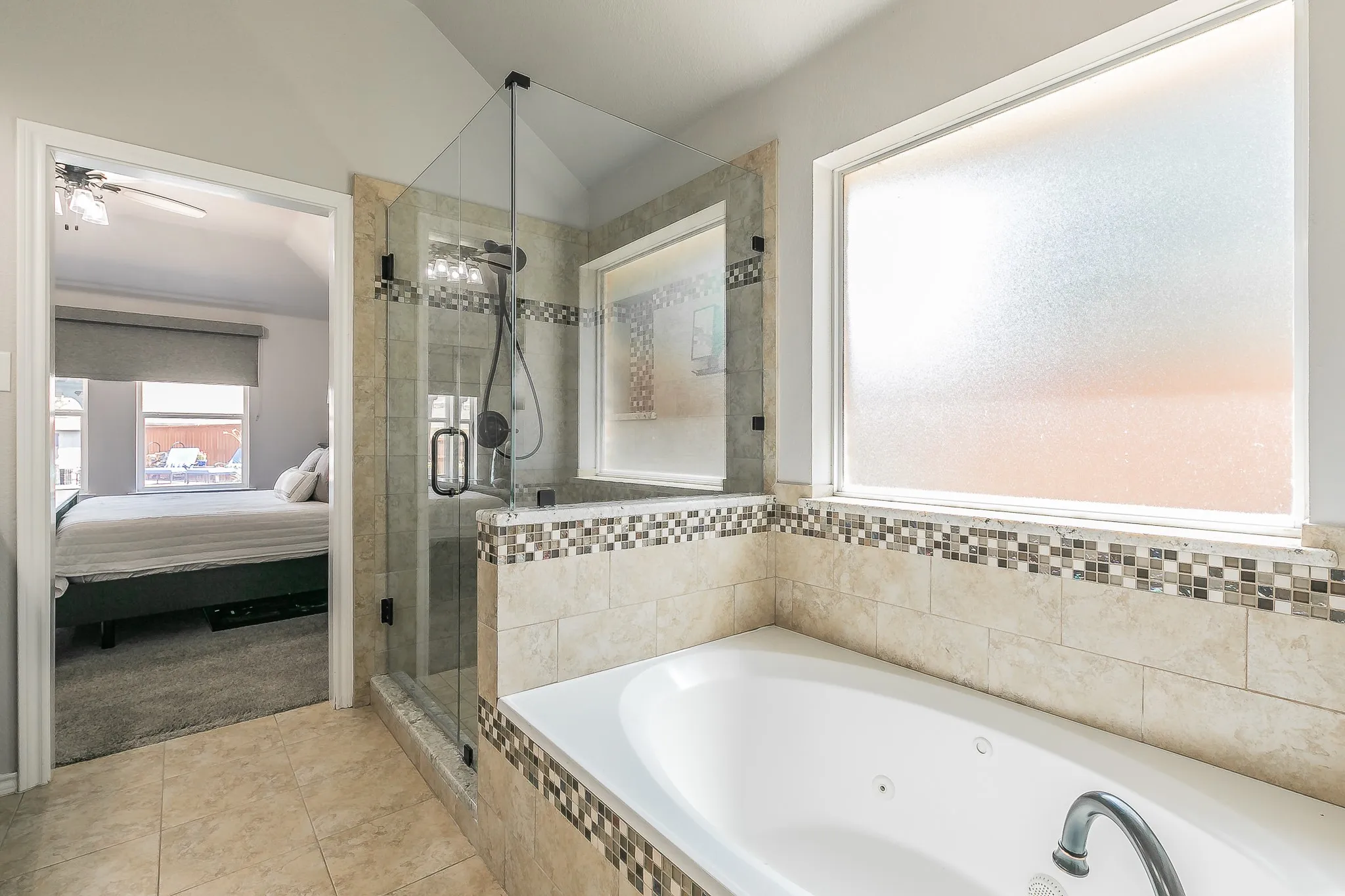 Jetted soaking tub with tile surround, glass-enclosed shower, and frosted privacy window