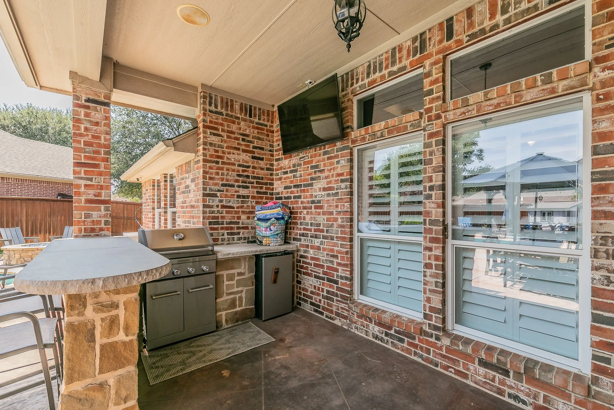 Covered patio featuring a built-in grill, stone bar, outdoor refrigerator, and brick exterior