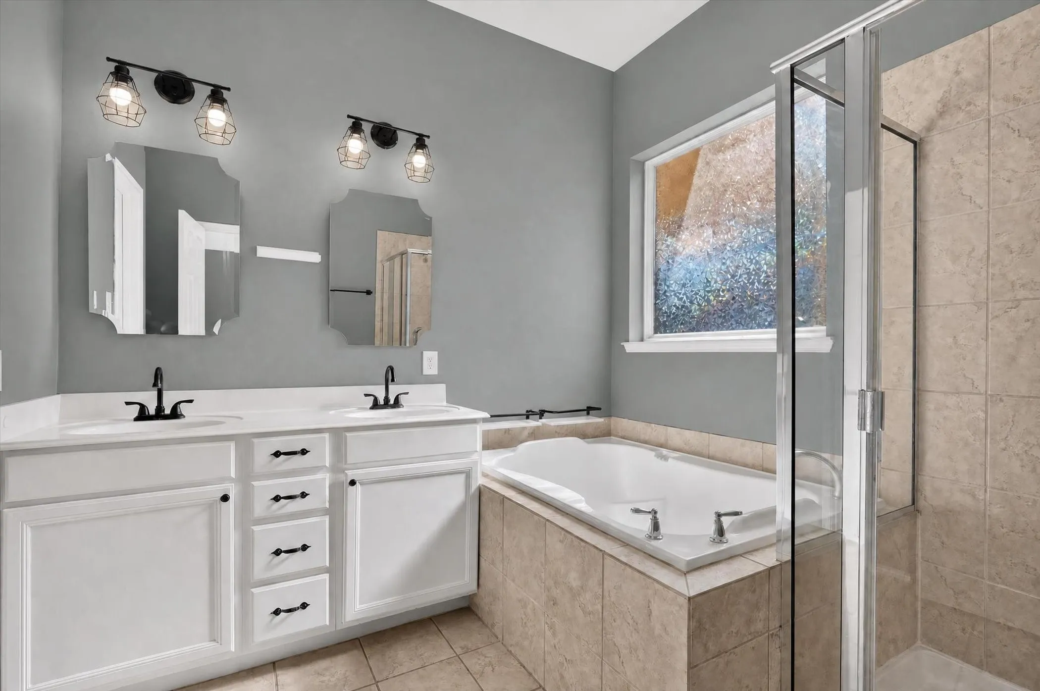 Dual vanity with white cabinetry and black hardware, separate soaking tub, and a glass-enclosed shower