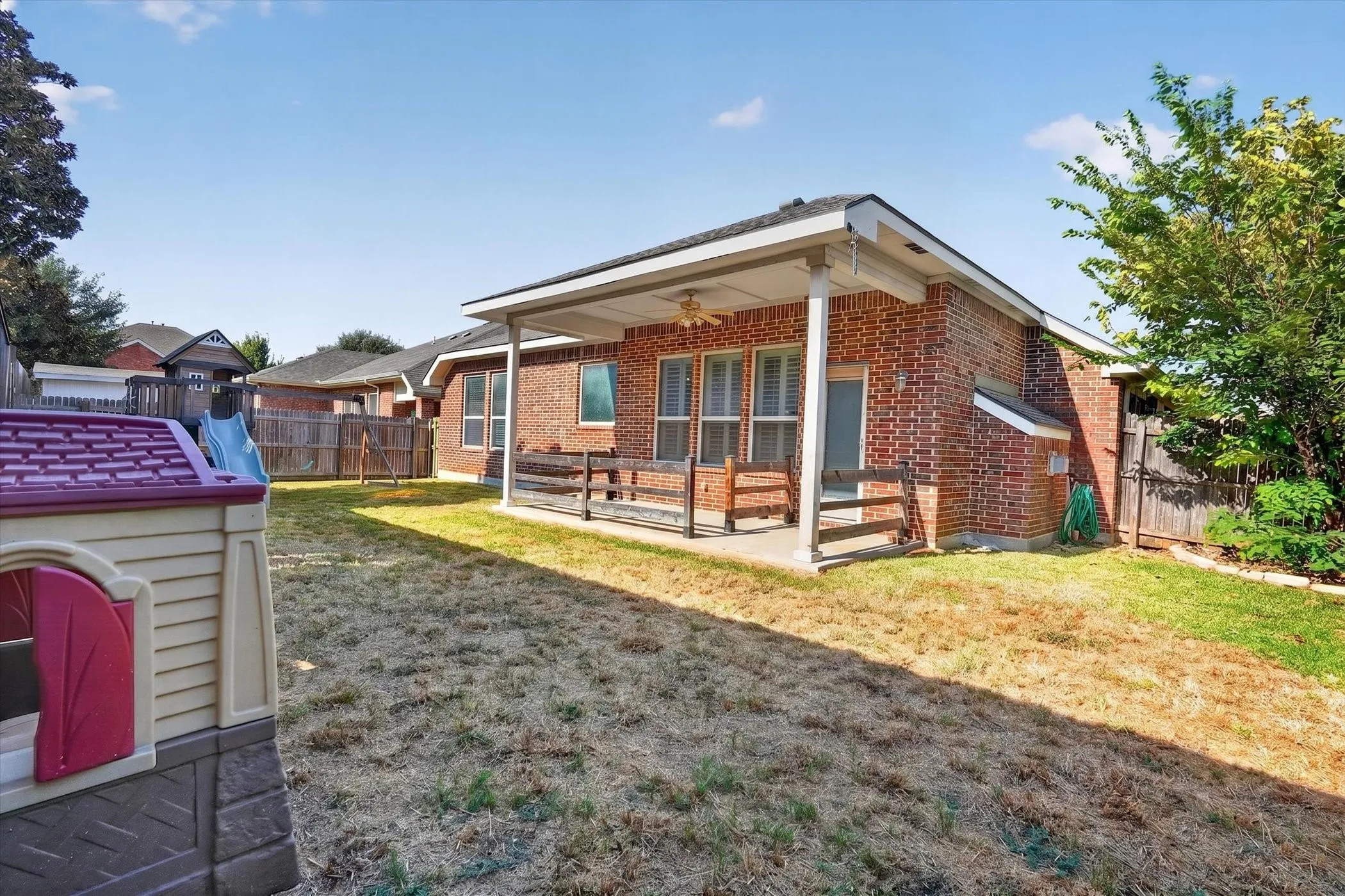 Brick exterior with a covered patio, ceiling fan, and fenced yard