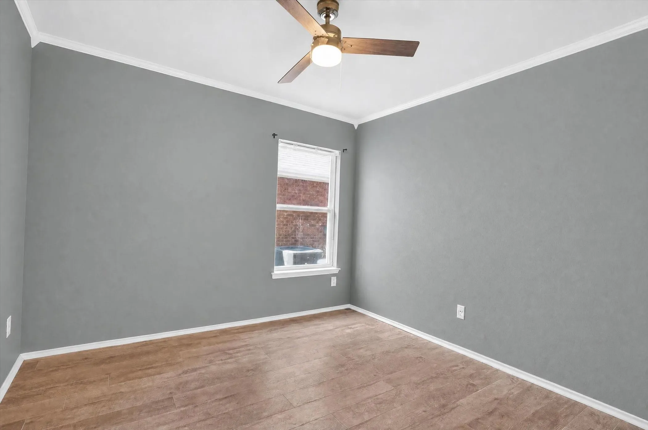 Wood-finish flooring, light gray walls, white crown molding, white window trim, and a ceiling fan with integrated lighting