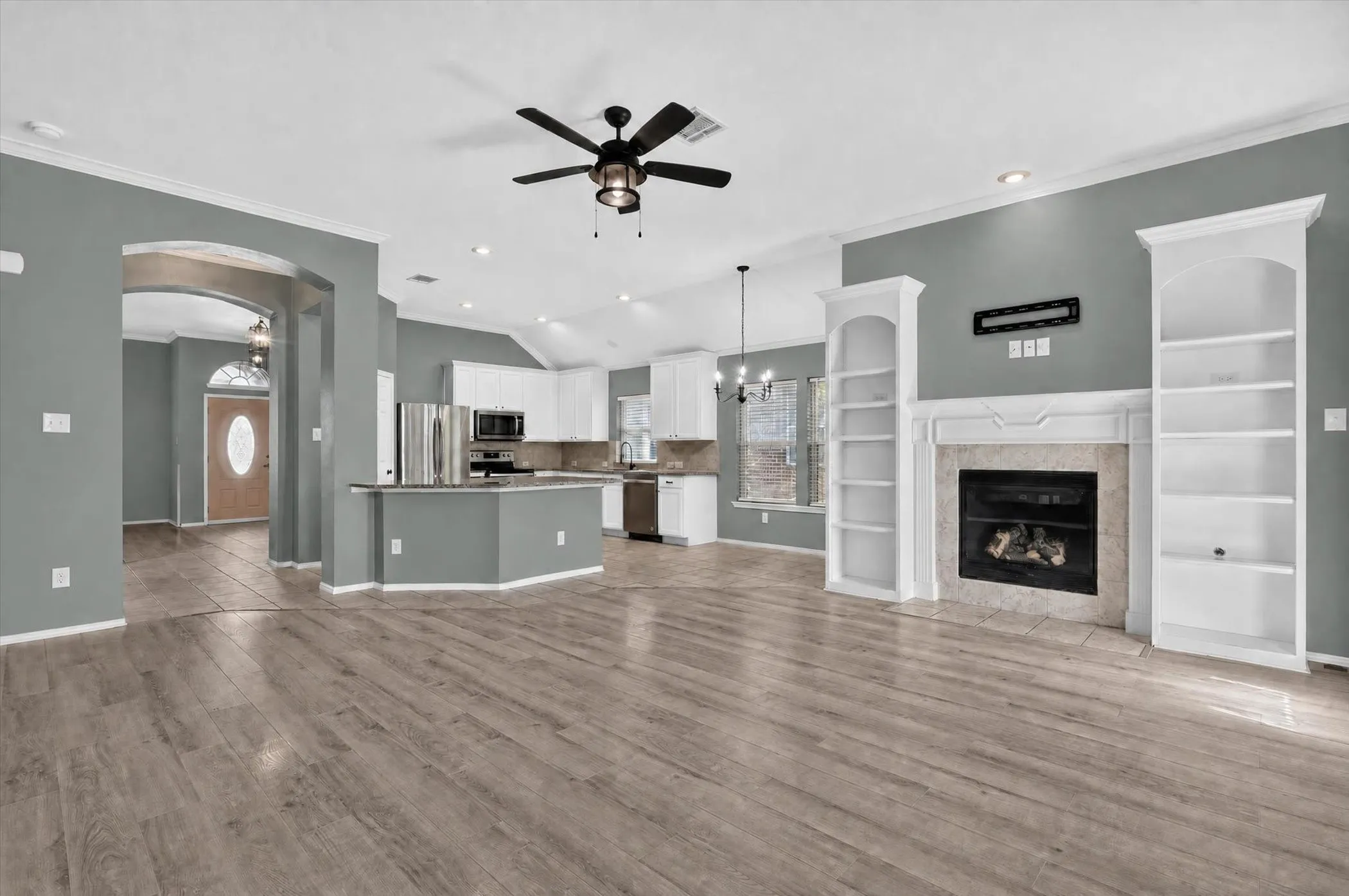 Expansive living area with wood-finish flooring, a fireplace with a stone surround, and built-in shelving