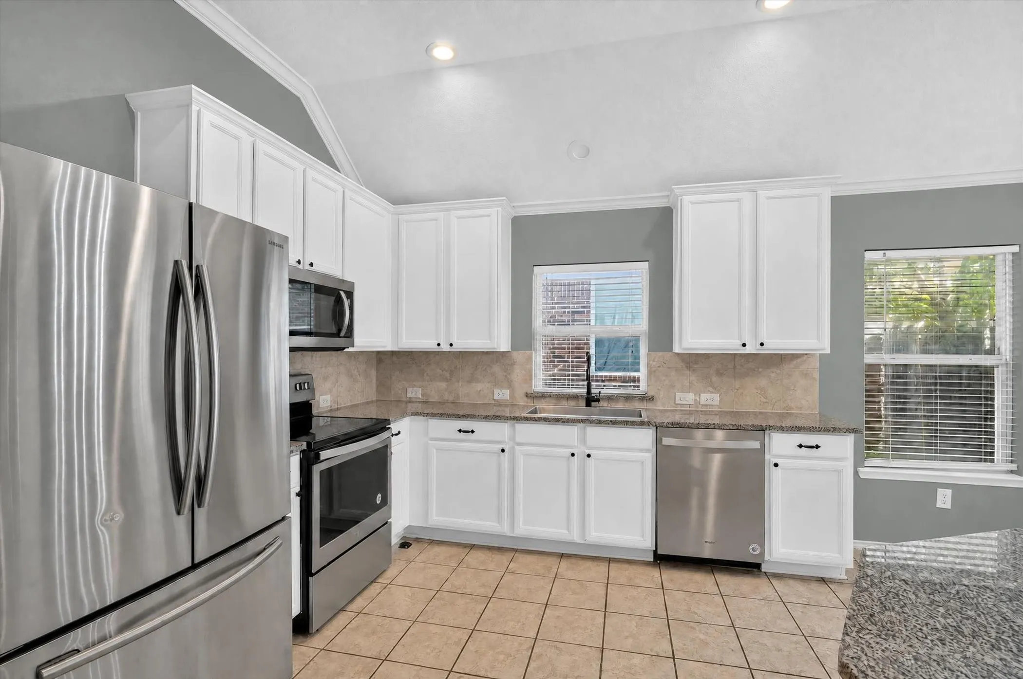 Kitchen with vaulted ceiling, white cabinetry, stainless steel appliances, tile flooring, and stone-look countertops