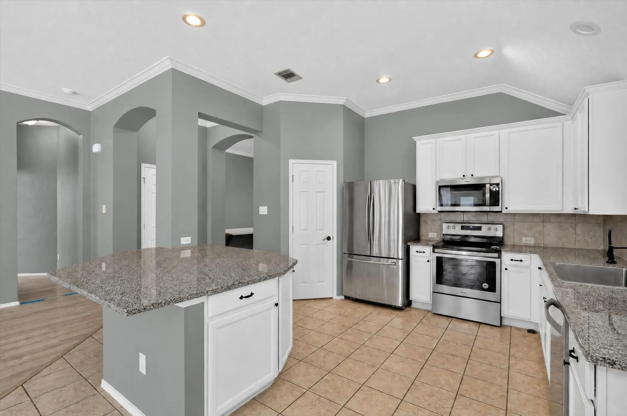 Kitchen featuring a center island with a granite countertop, white cabinetry, stainless steel appliances, and tile flooring