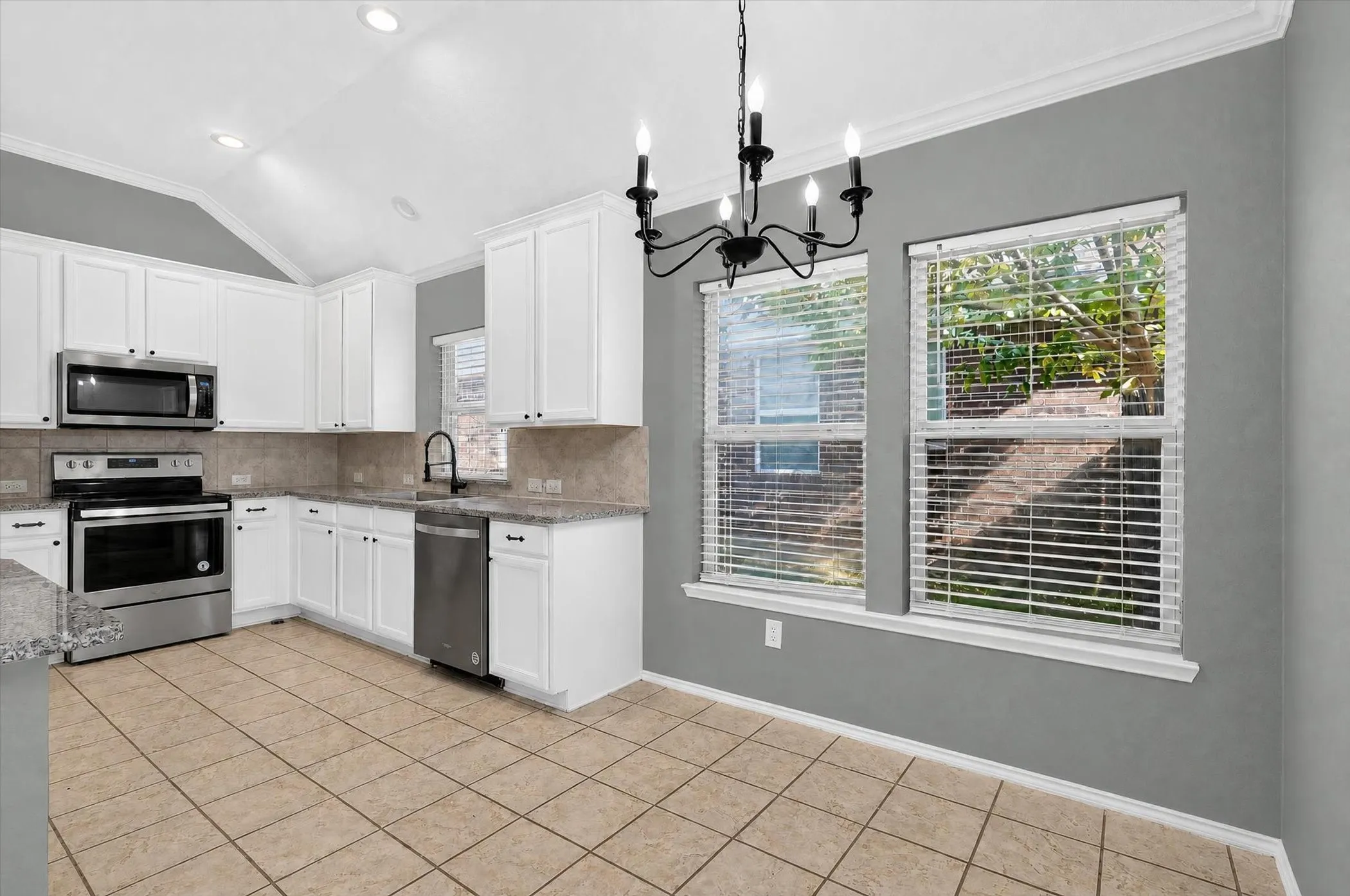 Kitchen featuring white cabinetry, stainless steel appliances, speckled countertops, tile flooring, and a chandelier