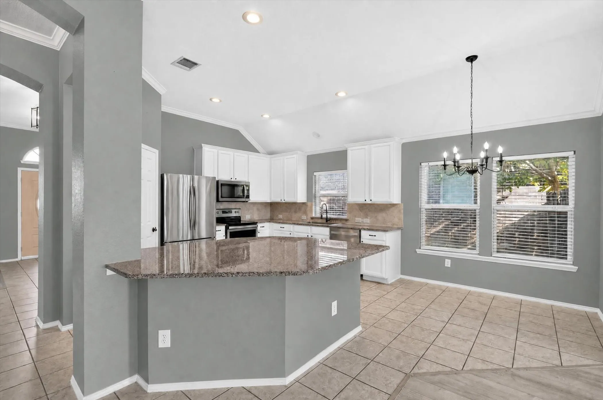 Open-concept kitchen featuring white cabinetry, stainless steel appliances, a breakfast bar, and tile flooring