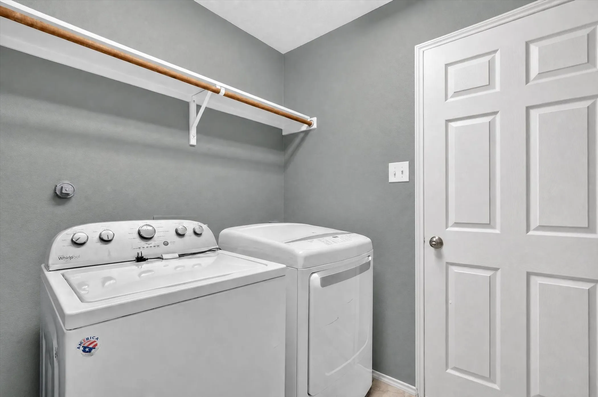 Laundry area featuring a mounted storage shelf with a wood rod and a paneled door