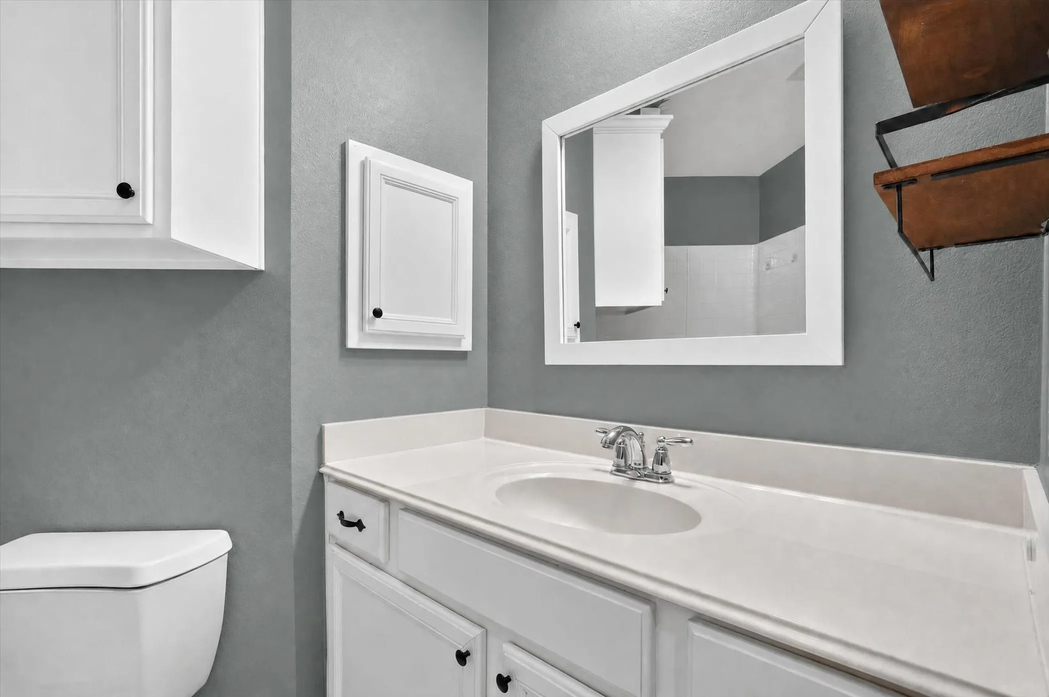 White framed mirror, white vanity with integrated sink, chrome faucet, and white overhead cabinetry