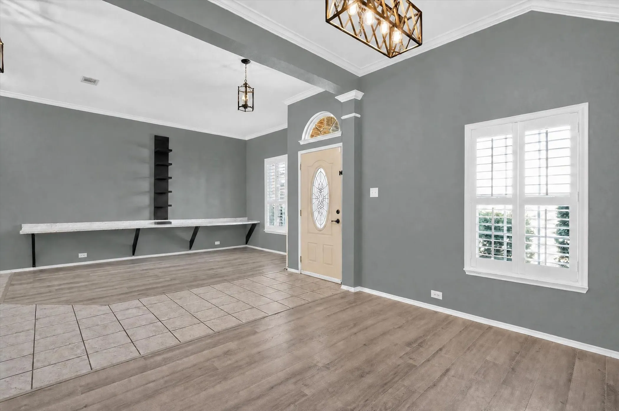 Spacious room featuring vaulted ceilings, decorative crown molding, and a combination of wood-finish flooring and tile